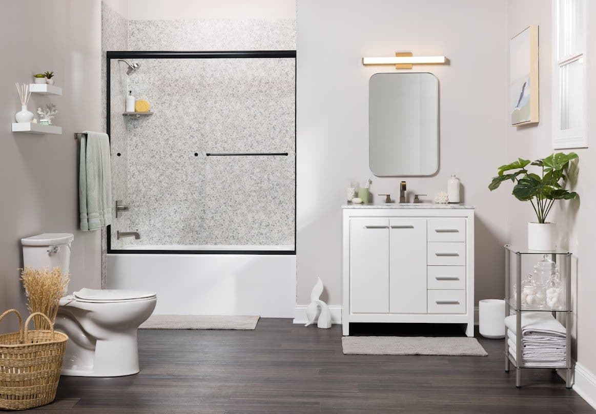 Modern bathroom with wooden floors, white vanity, and a potted plant. Shower has glass doors and a light gray tile. Bright and tidy ambiance.